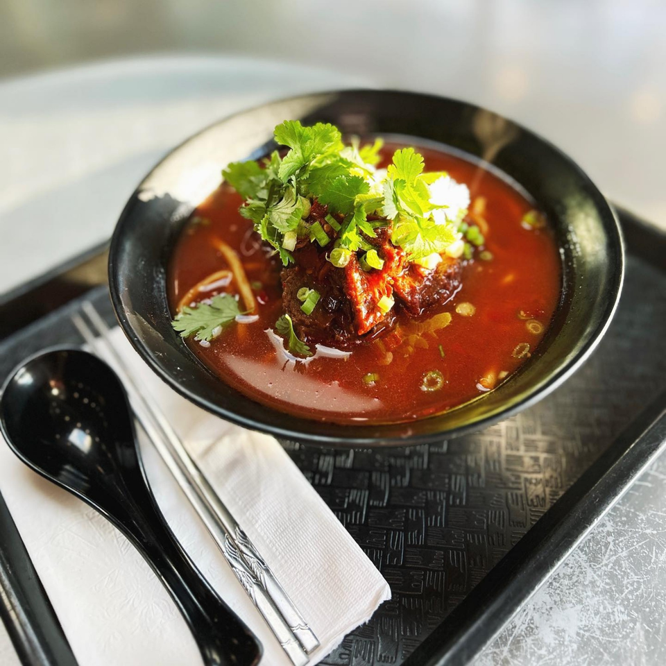 A black bowl of Asian beef noodle soup with cilantro and green onions on a tray.