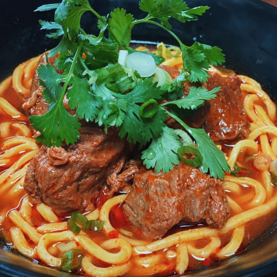 Close-up of a bowl of Asian noodles with beef, cilantro, and green onions in a spicy broth.