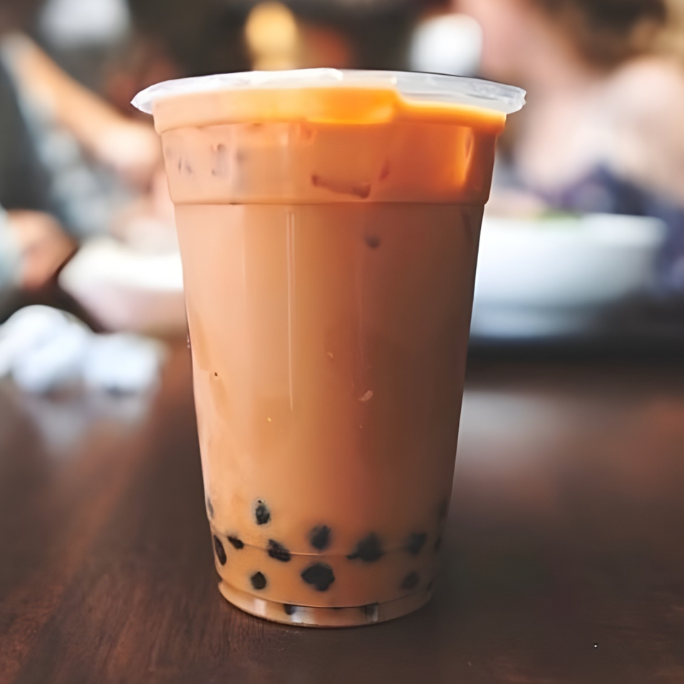 A plastic cup of Thai iced tea with tapioca pearls sits on a wooden table.