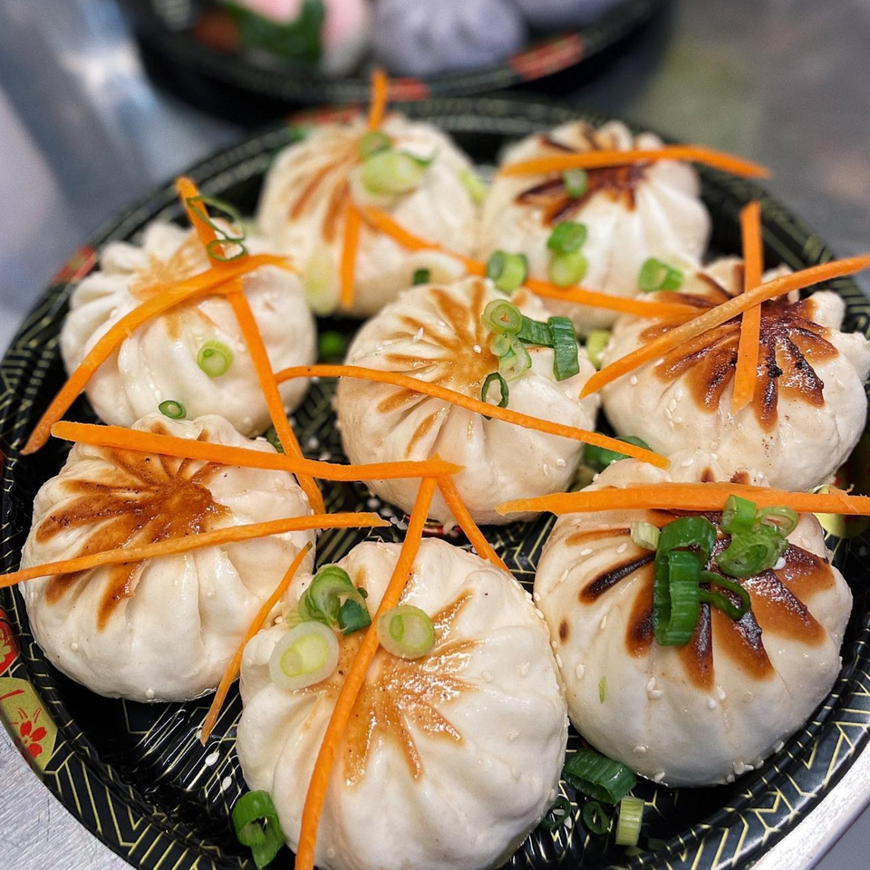 A platter of eight pan-fried dumplings, garnished with shredded carrots and chopped green onions.