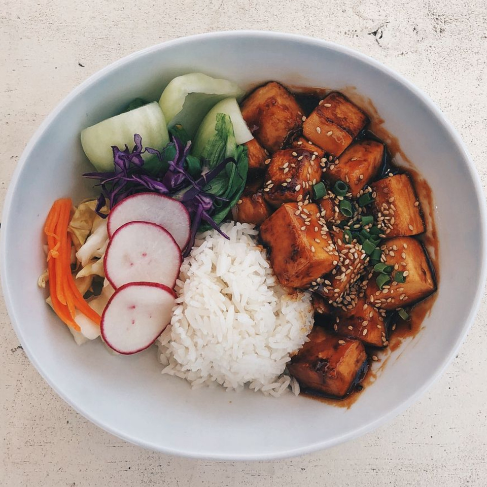 Asian dish with glazed tofu, white rice, sliced radishes, carrots, and green vegetables in a bowl.