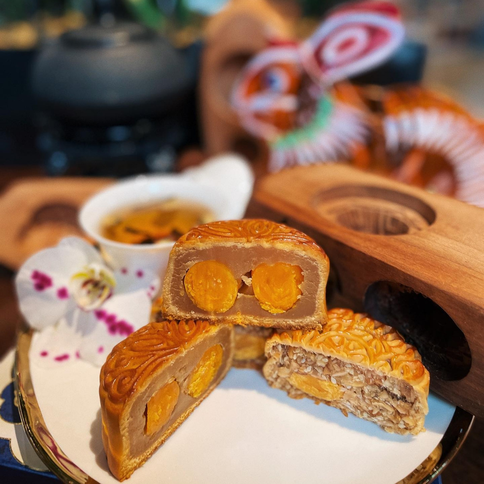 Mooncakes with various fillings, including salted egg yolks, on a white plate with tea and an orchid.